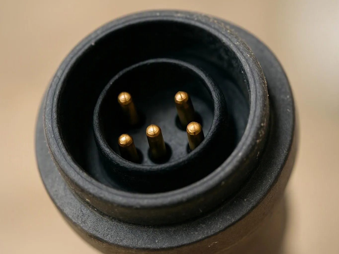 Close-up of a black circular connector with five gold pins against a beige background