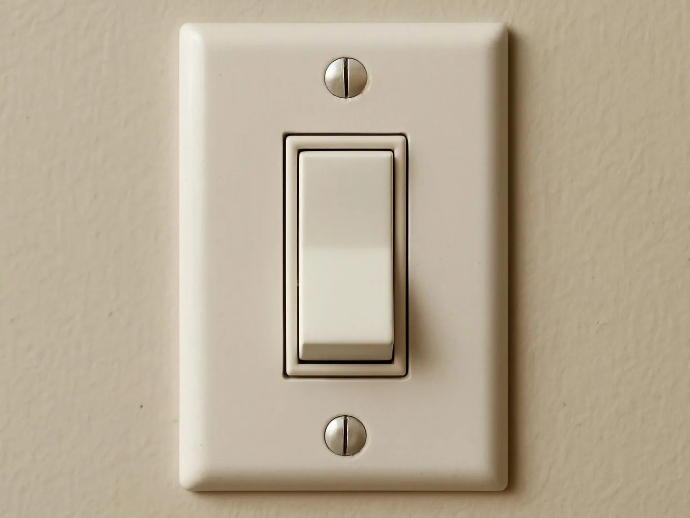 A white wall light switch plate with two screws sits on a beige painted wall